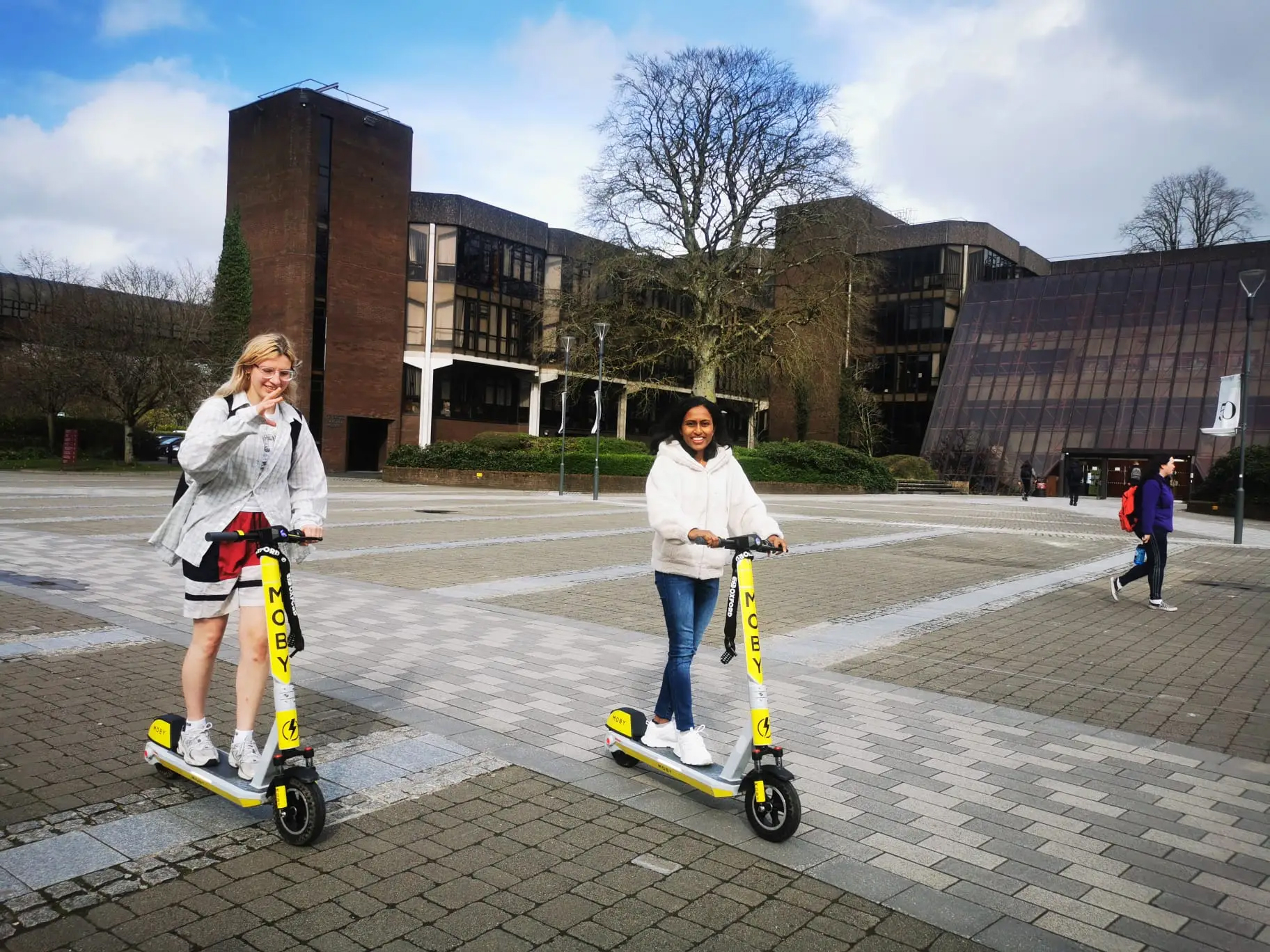 Two riders on yellow MOBY e-scooters on the University of Limerick campus plaza