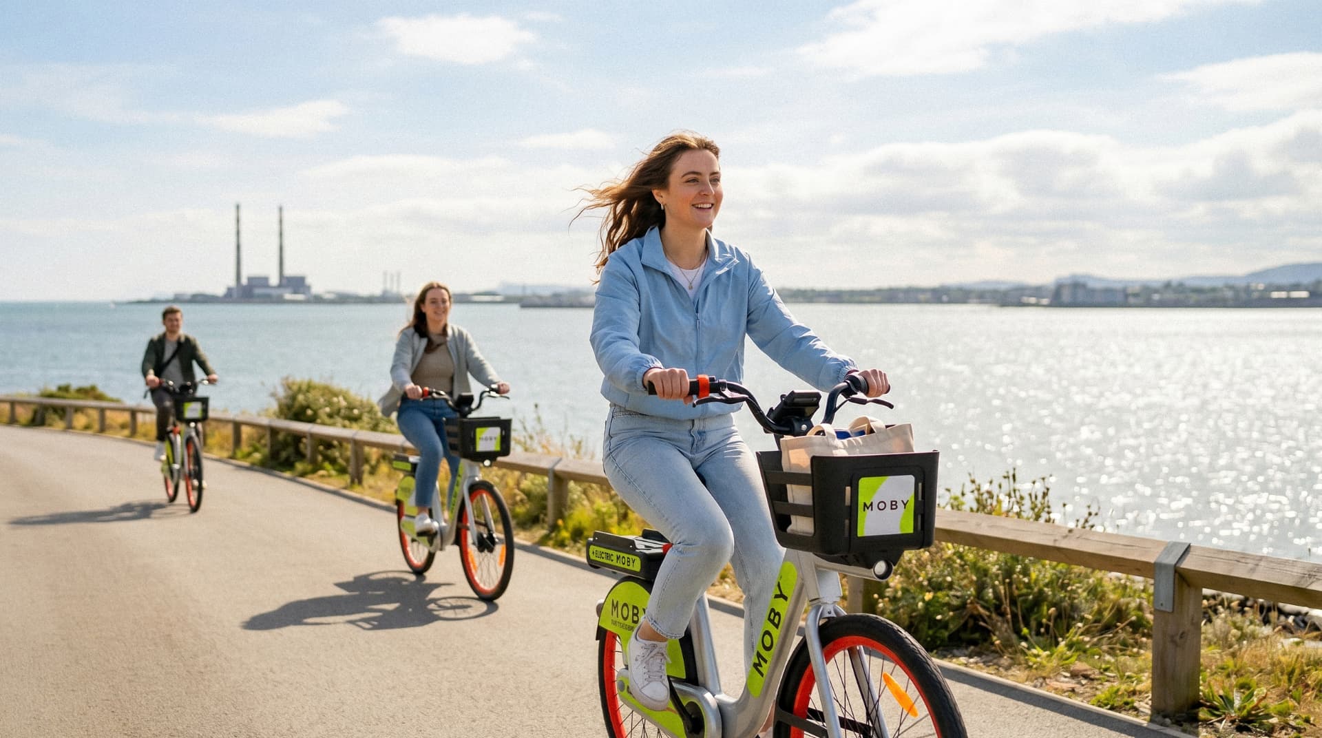 Three students riding MOBY e-Bikes along a coastal path by Dublin Bay