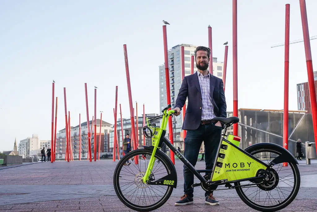 Thomas O'Connell, CEO and Founder of MOBY, standing with a neon-green MOBY e-bike on a Dublin plaza